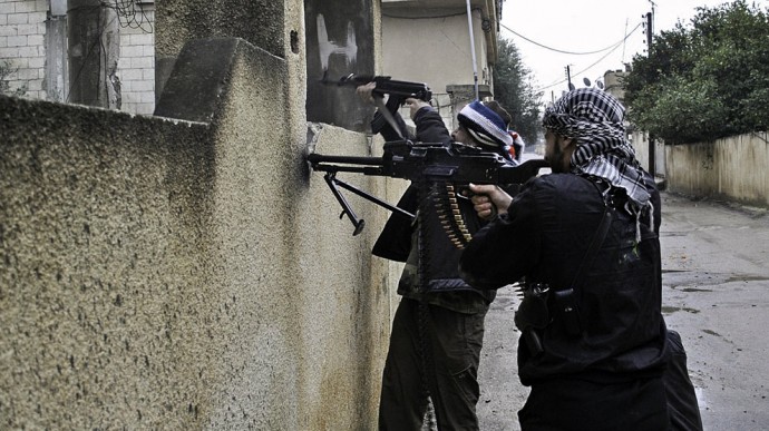 Syrian rebels take a position behind a wall as they fire their weapons during a battle with the Syrian government forces, at Rastan, in Homs province, Syria, on January 31, 2012 (Photo by Freedom House)