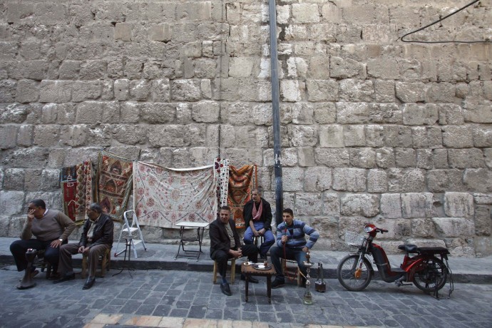 Tapestries are displayed as men sit outside the Omayyid mosque in old Damascus, Syria, Thursday, March 22, 2012. Mounting international condemnation of Bashar Assad's regime and high-level diplomacy have failed to ease the year-old Syria conflict, which the U.N. says has killed more than 8,000 people. (AP Photo/Muzaffar Salman)