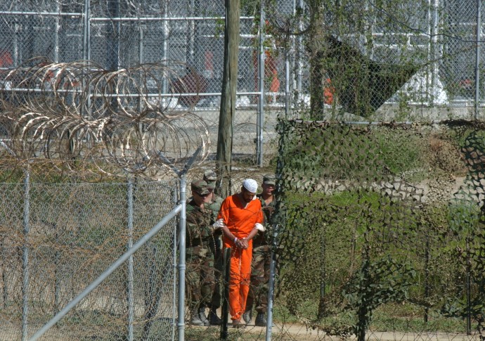 FILE - In this March 1, 2002 file photo, a detainee is escorted to interrogation by U.S. military guards in the temporary detention facility Camp X-Ray at the Guantanamo Bay U.S. Naval Base in Cuba. Open for 10 years on Wednesday Jan. 11, 2012, the Guantanamo Bay prison seems more established than ever. The deadline set by President Barack Obama to close it came and went two years ago. No detainee has left in a year because of restrictions on transfers, and indefinite military detention is now enshrined in U.S. law. Prisoners at the U.S. base in Cuba plan to mark the day with sit-ins, banners and a refusal of meals, said Ramzi Kassem, a lawyer who represents seven inmates. (AP Photo/Andres Leighton, File)