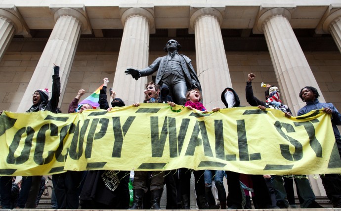 Occupy Wall Street demonstrators stand and cheer in front of the George Washington statue on Wall Street as they celebrate the protest's sixth month, Saturday, March 17, 2012, in New York. With the city's attention focused on the huge St. Patrick's Day Parade many blocks uptown, the Occupy rally at Zuccotti Park on Saturday drew a far smaller crowd than the demonstrations seen in the city when the movement was at its peak in the fall. A couple hundred people attended. (AP Photo/John Minchillo)