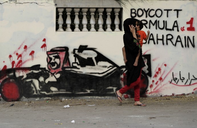 A Bahraini carrying a child passes a wall Thursday, April 5, 2012, in Barbar, Bahrain, west of the capital of Manama, that is painted with graffiti depicting Bahrain's King Hamad bin Isa Al Khalifa in a race car, calling for a boycott of this year's Formula One Bahrain grand prix, scheduled for April 22. The Arabic is a signature reading "free men of Barbar." A year after an anti-government uprising forced Bahrain's rulers to cancel the kingdom's coveted Formula One race, the grand prix is again smack in the middle of a power struggle. (AP Photo/Hasan Jamali)