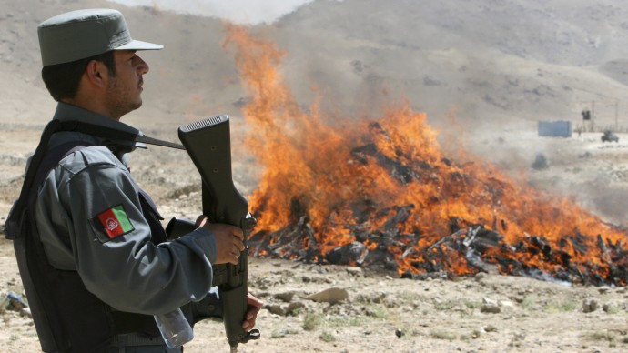 An Afghan security man hold his weapon as he stands in front of a flame of opium fire during an opium burning ceremony on the outskirts of Kabul, Afghanistan, Wednesday, June 25, 2008. (AP Photo/Rahmat Gul)