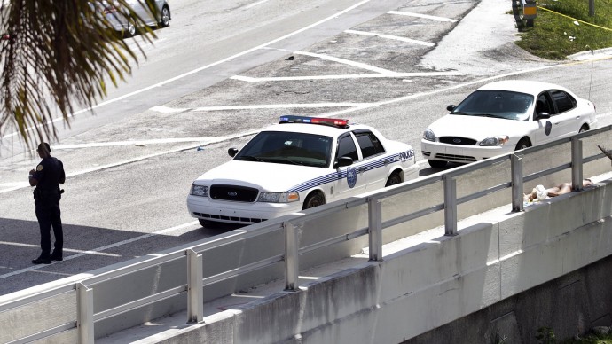 A City of Miami police officer stands watch near the scene where a naked man, far right, was shot dead on the MacArthur Causeway ramp onto Northeast 13th Street in Miami on Saturday, May 26, 2012. A witness said the naked man continued to chew on the face of another naked man on a Miami highway ramp and growled when a police officer tried to stop him. The victim remained hospitalized Monday. (AP Photo/The Miami Herald, Marsha Halper)