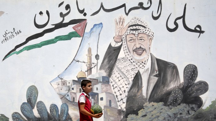 A Palestinian youth walks next to a mural depicting late Palestinian leader Yasser Arafat, in the northern West Bank village of Kabatyeh, Wednesday, July 4, 2012. Arabic text quotes a famous idiom meaning "We are holding to our promise." (AP Photo/Mohammed Ballas)
