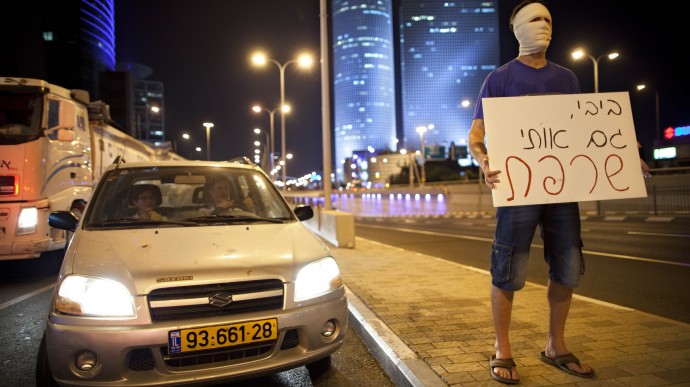 An Israeli man covers his face with a bandage as others, not seen, block a highway in Tel Aviv on Sunday, July 15, 2012, during a protest against the economic policies of Israel's government and to show solidarity with Moshe Silman, an Israeli protester who set himself on fire on Saturday during a protest. The sign in Hebrew reads: "Bibi you burned me too," referring to Israel's Prime Minister Benjamin Netanyahu by his nickname. (AP Photo/Oded Balilty)