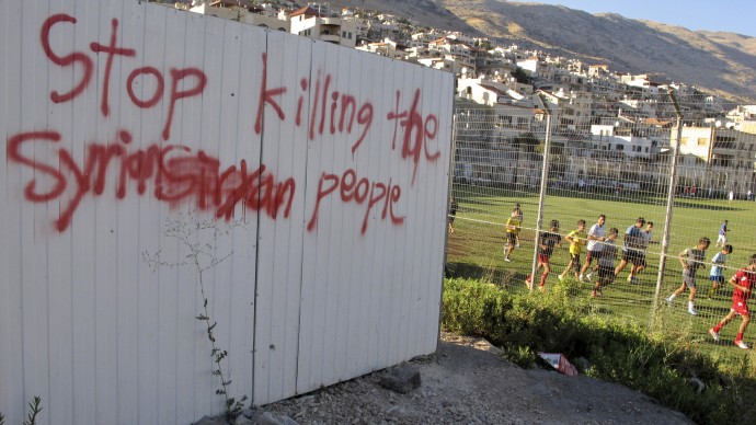 In this Wednesday, Aug. 8, 2012 photo, boys train in a soccer field next to a graffiti against the killing in Syria, in Majdal Shams, Golan Heights. (AP Photo/Diaa Hadid)