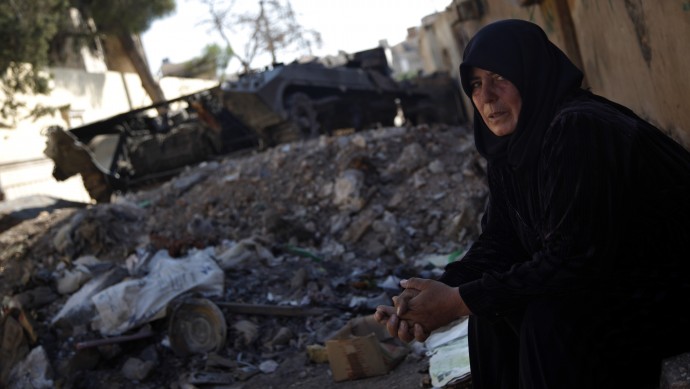 In this Sunday Aug. 5, 2012 photo, a Syrian woman looks on as she sits next to a destroyed military vehicle in the town of Atareb on the outskirts of Aleppo, Syria. (AP Photo)
