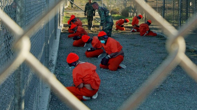 In this handout photo from the Department of Defense made available Friday Jan. 18, 2002, Taliban and al-Qaida detainees in orange jumpsuits sit in a holding area under the watchful eyes of military police at Camp X-Ray at Naval Base Guantanamo Bay, Cuba, during in-processing to the temporary detention facility on Jan. 11, 2002. (APPhoto/Shane T.McCoy, U.S. Navy)