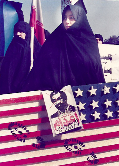 An Iranian woman holds the U.S. flag and a photo of Salman Rushdie, the author who wrote "The Satanic Verses" during a protest march in Tehran in February 1979. (Photo by Norbert Schiller/MintPress)