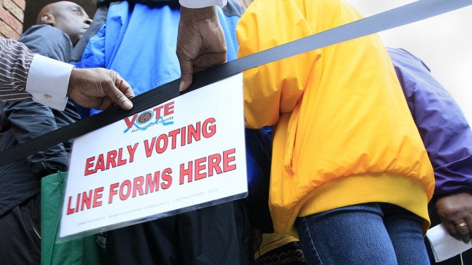 This Oct. 2, 2012 file shows a man placing a sign letting people know where to line up for early voting at the Hamilton County Board of Elections, in Cincinnati. (AP Photo/Al Behrman, File)