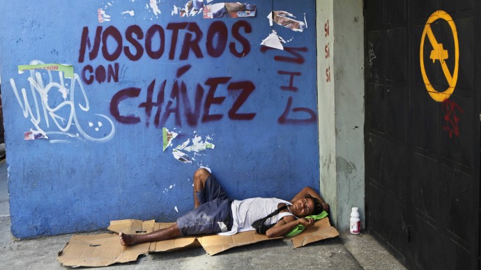 Homeless Efrain Juanipas, 37, rests on a makeshift bed made from a a cardboard box next to graffiti that reads in English: "We're with Chavez," in reference to Venezuela's President Hugo Chavez, in Caracas, Venezuela, Monday, Oct. 8, 2012. (AP Photo/Rodrigo Abd)