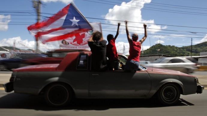 People ride atop a vehicle waving a Puerto Rican flag during elections in San Juan, Puerto Rico, Tuesday, Nov. 6, 2012. (AP Photo/Ricardo Arduengo)