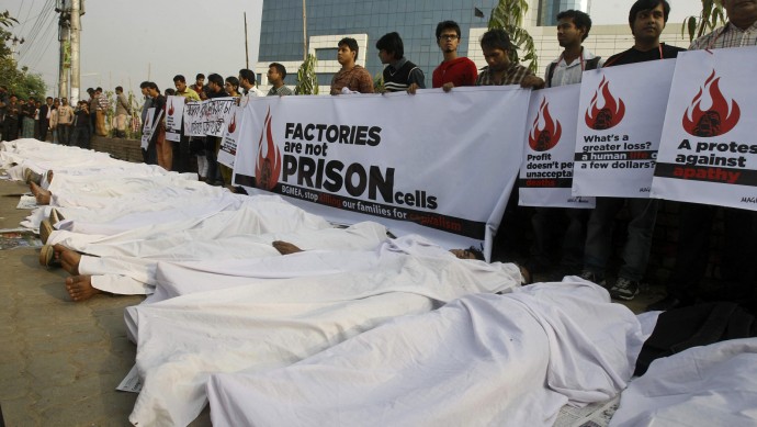 Bangladeshi protesters hold placards as some of them lie down on the ground posing as dead bodies as they condemn the death of workers in the weekend fire at a garment factory in Dhaka, Bangladesh, Wednesday, Nov. 29, 2012. (AP Photo/Pavel Rahman)