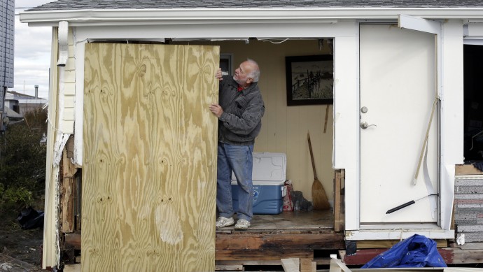 Chuck Clauser prepares to hang a sheet of plywood to cover a hole where a wall once stood before his house was damaged by surge from Superstorm Sandy on Cedar Bonnet Island, N.J., Saturday, Nov. 3, 2012. (AP Photo/Patrick Semansky)