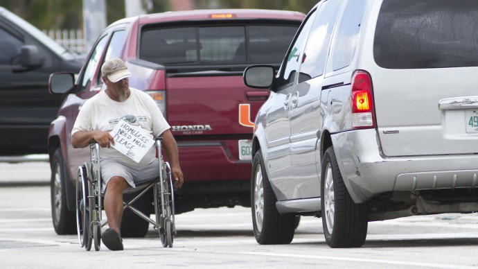 An unidentified disabled man rolls his wheelchair between cars on a Miami exit ramp Thursday, Sept. 16, 2010, displaying a sign that says he is homeless. (AP Photo/J Pat Carter)