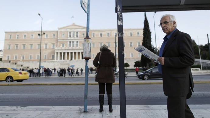 A man reads a newspaper as he walks past a bus stop opposite the Parliament in central Athens, Tuesday, Nov. 27, 2012. (AP Photo/Petros Giannakouris)