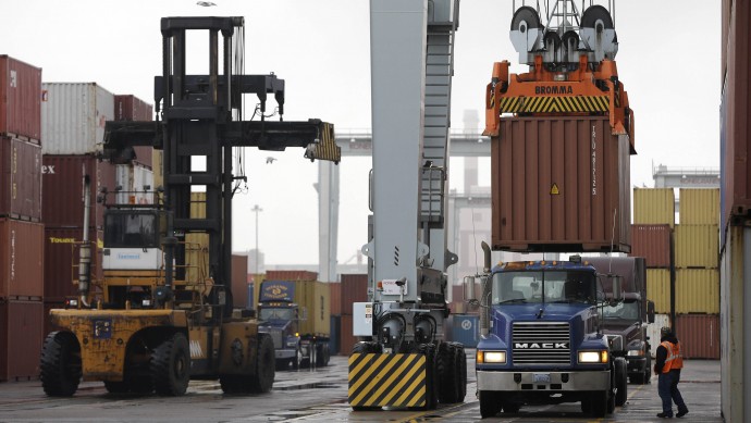 In this Dec. 18, 2012 file photo, a truck driver watches as a freight container, right, is lowered onto a tractor trailer by a container crane at the Port of Boston in Boston. (AP Photo/Steven Senne, File)