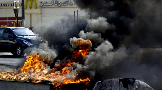 Vehicles pass by tires and old water storage tanks set on fire by Bahraini anti-government protesters in Malkiya, Bahrain, Monday, Dec. 17, 2012. (AP Photo/Hasan Jamali)