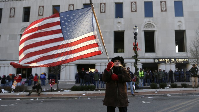 Protester Paula Merwin, of Leslie, Mich., stands with an American flag outside the George W. Romney State Building, Tuesday, Dec. 11, 2012. (AP Photo/Paul Sancya)