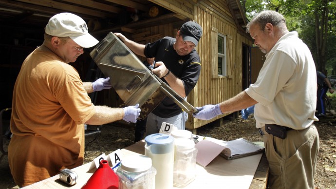 In this Sept. 2, 2010 file photo, Franklin County Detective Jason Grellner, center, sorts through evidence with Detective Darryl Balleydier, left, and reserve Officer Mark Holguin during a raid of a suspected meth house in Gerald, Mo.  (AP Photo/Jeff Roberson, File)